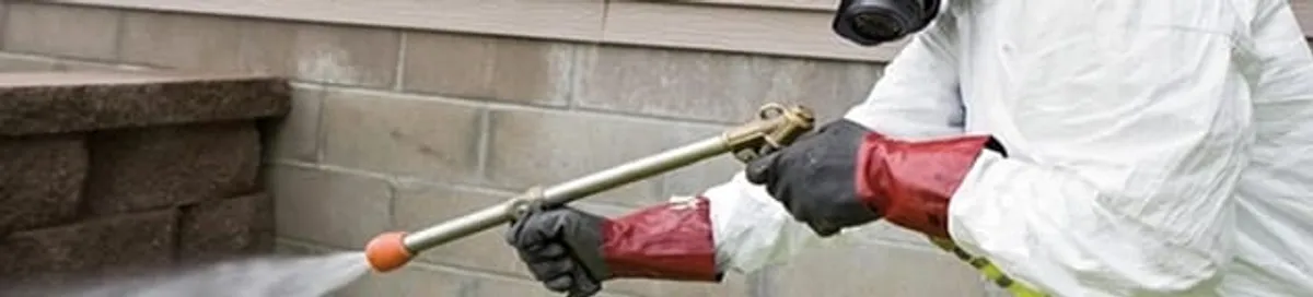 Pest control technician applying exterior insect treatment along a home foundation in Riverside, CA