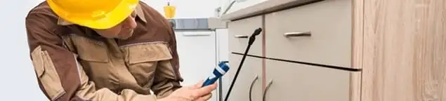 Roach exterminator applying treatment under kitchen cabinets in Riverside, CA