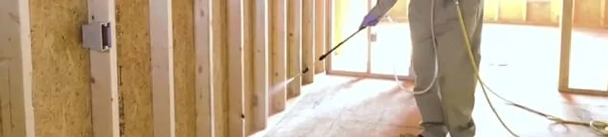 Termite treatment technician applying spray along framing and unfinished walls in Riverside, CA