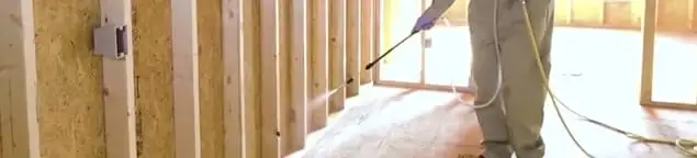Termite treatment technician applying spray along framing and unfinished walls in Riverside, CA